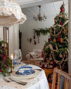 a dining room table set for christmas with plates and silverware in front of a decorated christmas tree