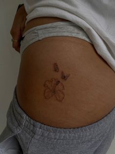 a woman's stomach with a butterfly and flower tattoo on the side of her belly