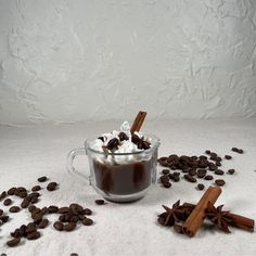 hot chocolate with marshmallows and cinnamon sticks in a glass mug surrounded by coffee beans