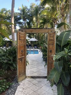 an open wooden door leading to a swimming pool surrounded by palm trees and greenery