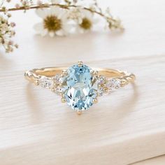 a ring with an oval blue topaz surrounded by small white diamonds on a wooden surface