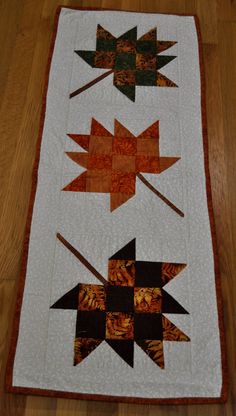 a quilted table topper with four different designs on it, including two leaves and one star