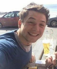 a man sitting at a table with a glass of beer in front of him smiling