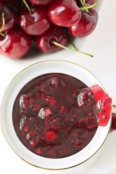 a white bowl filled with cherries next to a pile of cherries