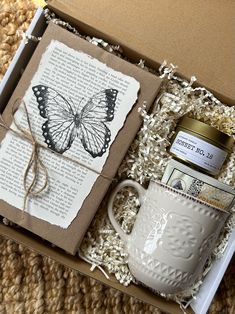 an open box containing a cup, jar and book with a butterfly on the lid