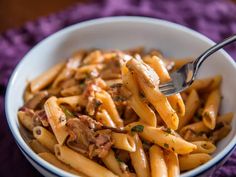 a bowl filled with pasta and meat on top of a purple table cloth next to a fork