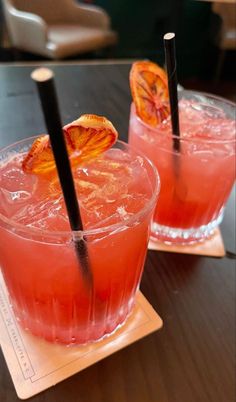 two glasses filled with blood orange juice and black straws on top of a wooden table