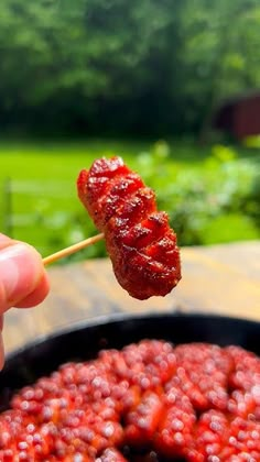 a person holding a skewer of food over a pan filled with strawberries