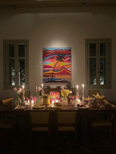 a dining room table is set with candles and flowers in front of a painting on the wall