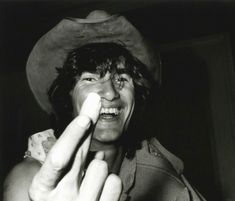 a black and white photo of a man wearing a cowboy hat pointing to the side