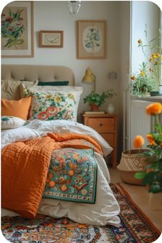 a bed with an orange blanket on top of it next to a vase filled with flowers