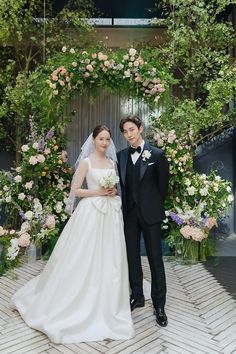 a man and woman standing next to each other in front of a flower covered archway