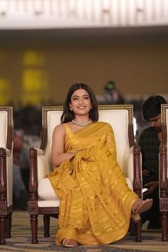 a woman in a yellow sari sitting on a white chair and smiling at the camera