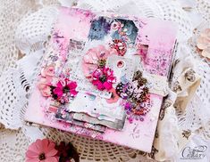 an altered book with pink flowers and lace on the table next to some crocheted doily