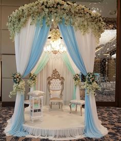 a white and blue wedding ceremony setup with draping, flowers, and chairs