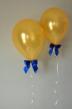 two yellow balloons with blue bows on them