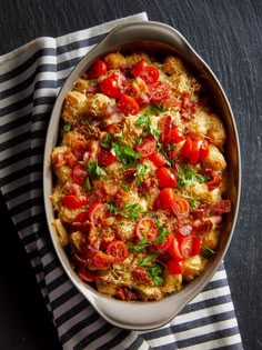 a casserole dish with tomatoes and parsley in it on a striped cloth