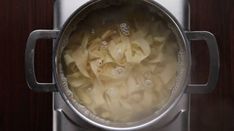 a pot filled with pasta and water on top of a wooden table next to a stove