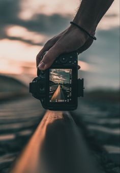 a person holding a camera up to take a photo with the sun setting in the background