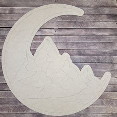 a paper cut out of the shape of a crescent with mountains in the background on a wooden surface