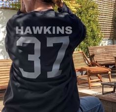 a woman sitting on top of a wooden bench wearing a black shirt with the number 37 printed on it