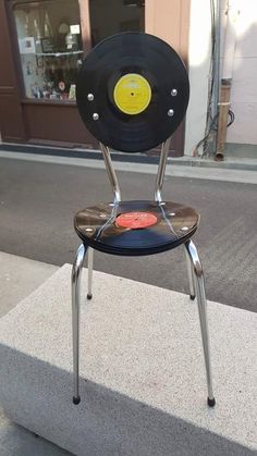 a chair made out of an old record with a yellow disc on the back sitting in front of a store