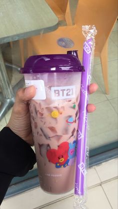 a person holding up a plastic cup with a purple straw in it