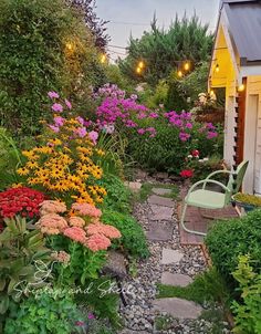 a garden with lots of flowers next to a white building and lights strung from the roof