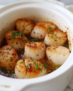 some cooked scallops are in a white pot with water and garnishes