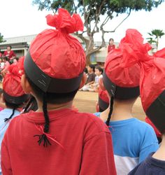 several children wearing red turbans standing in front of a group of people with their backs to the camera