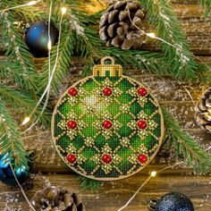 a cross stitch christmas ornament hanging from a pine tree with ornaments around it