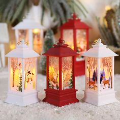 three red and white christmas lanterns with deers in the woods on them sitting on snow covered ground