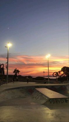 a skateboard park at sunset with the sun setting in the background and people riding their bikes