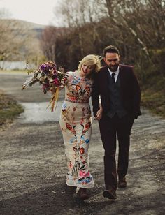 a man and woman walking down a dirt road holding hands with each other, both dressed in floral prints