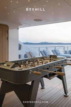 A dark gray outdoor football table with wooden handles set on a wooden deck of a luxurious yacht