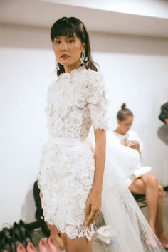 a woman standing in front of a row of shoes wearing white dress with flowers on it