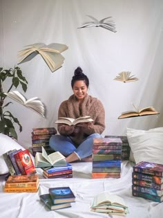 a woman is sitting on the bed with many books in front of her and reading