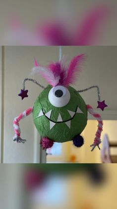 a green ball with pink hair and eyes hanging from it's side in front of a mirror