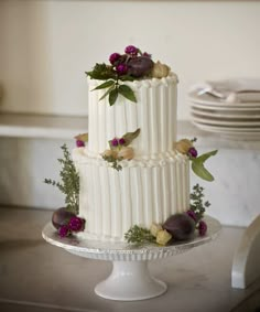 a three tiered white wedding cake with flowers on the top and bottom, sitting on a table in front of plates