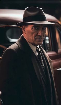 a man in a suit and hat standing next to a car