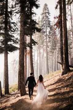 a bride and groom walking through the woods