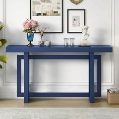 a blue console table with flowers and pictures on the wall