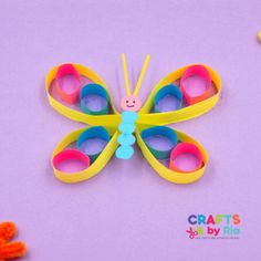 a colorful butterfly made out of paper on a purple surface with crayons around it