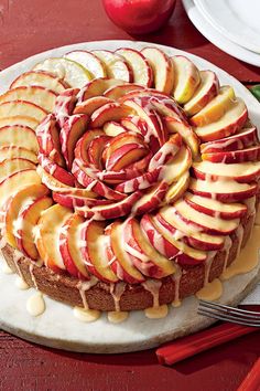 an apple cake with white icing and sliced apples on top, sitting on a plate