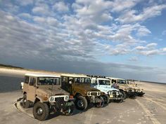 several jeeps are lined up on the beach in front of some water and clouds