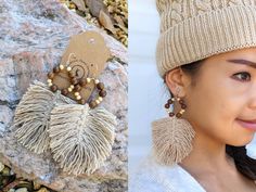 a woman wearing earrings and a hat next to a rock