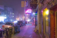 a city street at night with cars parked on the sidewalk