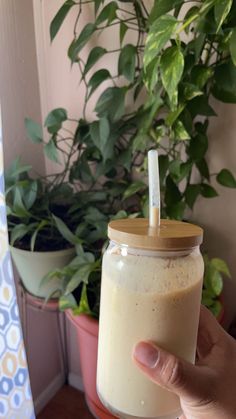 a hand holding a glass with a straw in it next to a potted plant