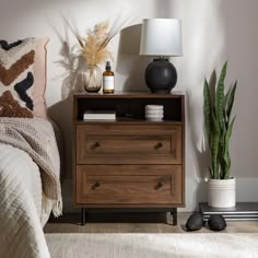 a bedroom with a bed, nightstand and potted plant on the side table next to it