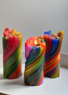 three multicolored candles sitting on top of a white table next to each other